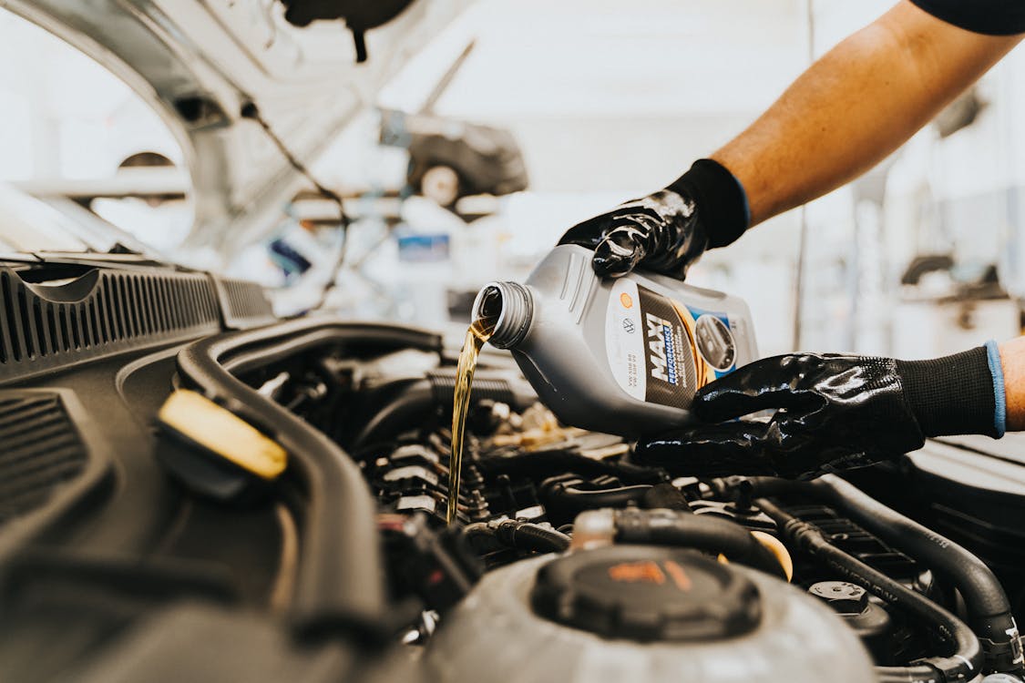 Mobile mechanic pouring fresh motor oil into a car engine during an on-site oil change service